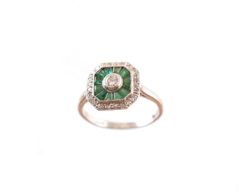 A platinum emerald and diamond dress ring, designed as a brilliant cut diamond collet within a calibré cut emerald and single