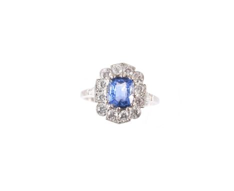 A sapphire and diamond cluster ring, the cushion shape sapphire within a brilliant cut diamond surround and baguette cut diam
