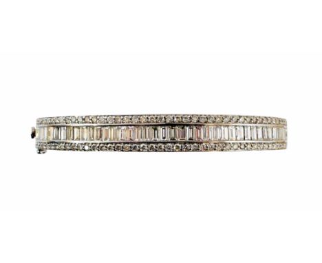 A diamond hinged bangle, the baguette cut diamond line with brilliant cut diamond sides and plain polished reverse, stamped K