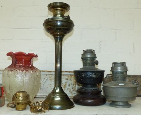 A brass reeded column oil lamp with cranberry edged shade; 2 other oil lamps; a shell case