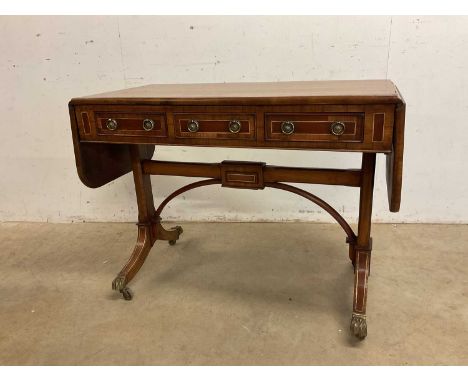 A Regency style sofa table with three frieze drawers raised on shaped end supports to brass paw feet and castors, width 99cm.