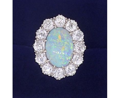 A large platinum opal and diamond cluster ring, the opal 12mm x 9mm, the twelve brilliant cut diamonds approx. 4mm diameter, 