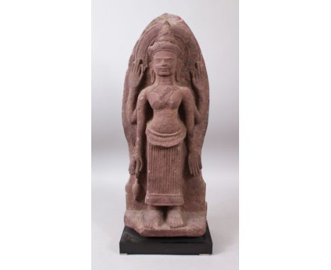 A 12TH CENTURY STYLE CAMBODIAN KHMER STYLE RED SANDSTONE CARVING OF A FOUR ARMED DEITY. 52cms high.