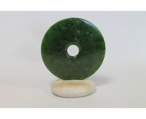 Green jade pierced disc set in a marble pebble base, 17cm diameter.