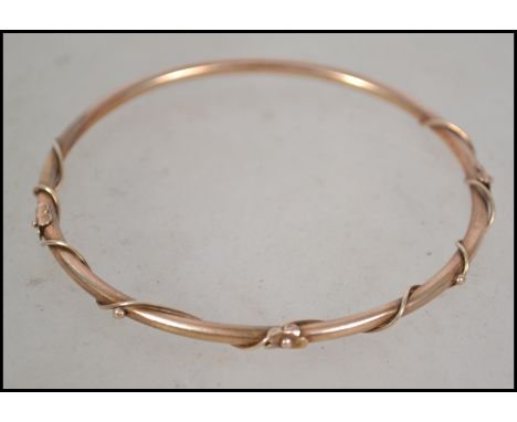 A 9ct gold slave bangle with applied vine and flower head twist surround. The inside of the bangle being hallmarked &nbsp;but