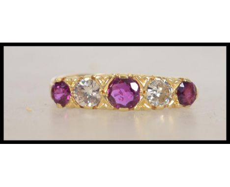 A hallmarked 18ct gold, ruby and diamond ring set with two round cut diamonds and three round cut rubies in a scrolled galler