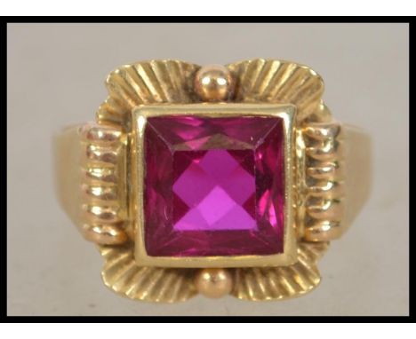 A early 20th century Art Deco 18ct gold ring set with a square cut ruby in an Egyptian revival style setting. &nbsp;Mark to s