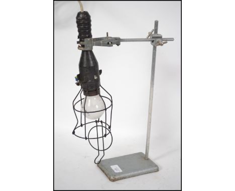 An up-cycled table lamp constructed from a vintage cast metal laboratory stans surmounted with a vintage caged inspection lam