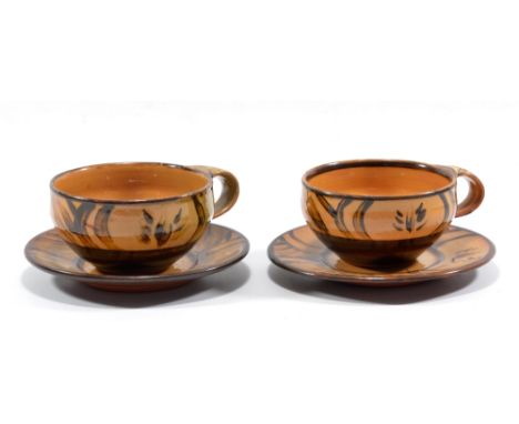 MICHAEL CARDEW (1901-1983) for Winchcombe Pottery; a near pair of slipware cups and saucers, iron decoration on dark ochre gr