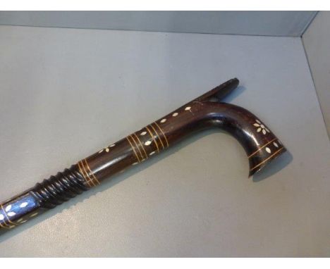 A carved hardwood walking stick with mother of pearl inlay. 