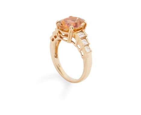 A topaz and diamond ring claw-set with an oval-shaped pinkish-orange topaz, each stepped shoulder set with baguette-cut diamo