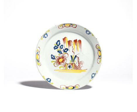 A Bristol delftware plate  c.1730, of primitive shape, painted in blue, green, red and yellow, with a large flowering plant b