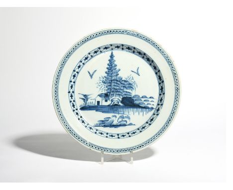 A delftware charger  c.1750, painted in blue with tall pine trees above a low hut, the cavetto with a diaper design, the rim 