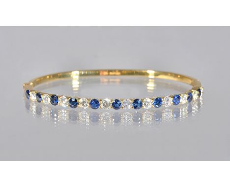 An 18ct gold, sapphire and diamond oval hinged bangle, claw set with a row of circular cut diamonds alternating with circular