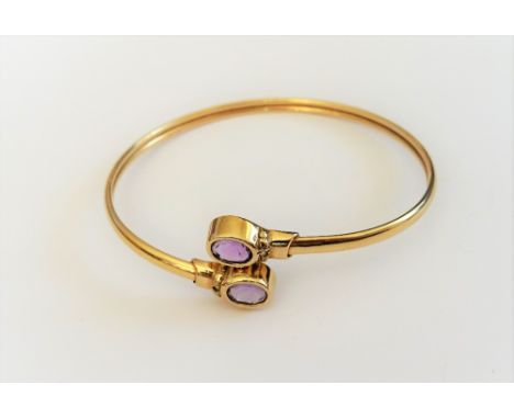 A 9ct gold and amethyst bangle, collet set with two oval cut amethysts, in a twistover design, gross weight 6.8 gms.