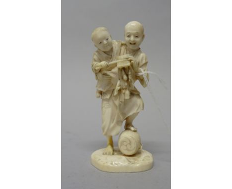 A Japanese ivory okimono, Meiji period, carved as a man carrying a child under his arm who holds a puppet, signed, 12cm. high