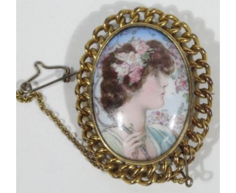 A porcelain plaque brooch, depicting a half length portrait of a lady in green dress, surrounded by flowers, in a gold plated