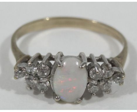 A dress ring, set with opal and flanked by ten tiny white stones, each claw set, on an unmarked yellow metal band. 