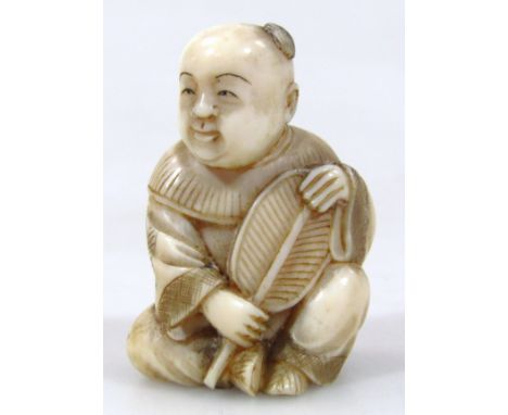 A Japanese carved ivory netsuke, of a seated baby boy holding a fan, 4.1cm long.(Taisho period 1912-1926) Provenance: Part of