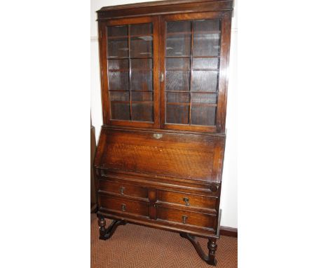 A 1920's oak bureau bookcase, the upper section with a moulded caddy top above glazed cupboard revealing bookshelves above a 