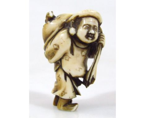 A Japanese carved and stained ivory netsuke, of a standing man holding a sack over his shoulder with a rat perched on top, si