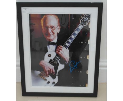 A framed & glazed coloured photograph of Les Paul playing a guitar signed by Les Paul in blue marker