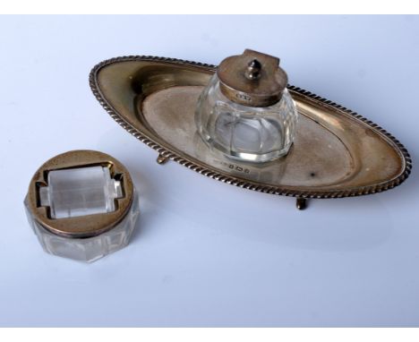 A silver mounted clear glass ink stand and a stamp roller; the oval stand with a central removable facetted glass ink well, a