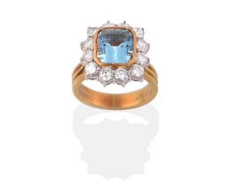 An 18 Carat Gold Aquamarine and Diamond Cluster Ring, an emerald cut aquamarine in a yellow rubbed over setting, within a bor