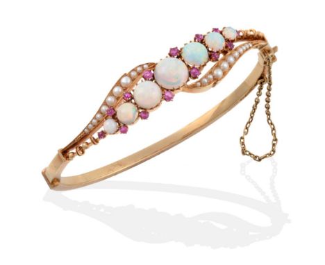 An Opal, Ruby and Seed Pearl Bangle, graduated round cabochon opals spaced by pairs of round cut rubies, set on a twist, with