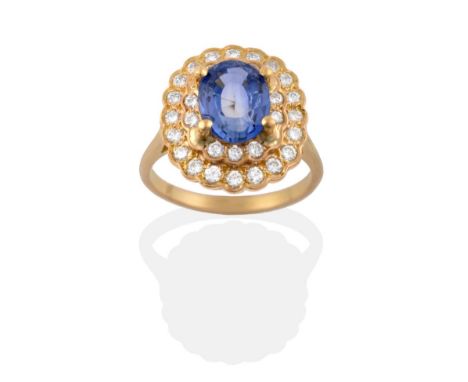 A Sapphire and Diamond Cluster Ring, an oval mixed cut sapphire in a yellow four claw setting, within a double stepped border