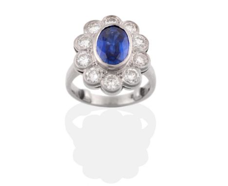 A Platinum Sapphire and Diamond Cluster Ring, the oval mixed cut sapphire in a rubbed over setting within a border of round b