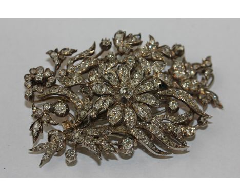 A Victorian diamond brooch with a ten panelled flower head in tremblant amongst leaves and smaller flowers set throughout wit