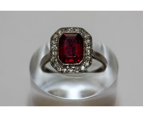 A ruby and diamond ring the step cut stone rubover set within a border of eight cut diamonds in plain platinum mount