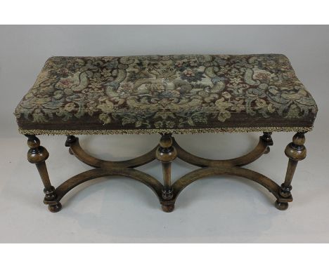 A long stool of William and Mary style with deer, dog and floral tapestry seat, on turned legs tied by flat shaped stretcher 