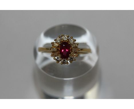 A ruby and diamond cluster ring oval cut within a border of baguette and brilliant cut diamonds in 18ct gold