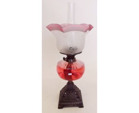 A Victorian oil lamp with cast iron base, clear glass reservoir and etched shade with cranberry reeded edge