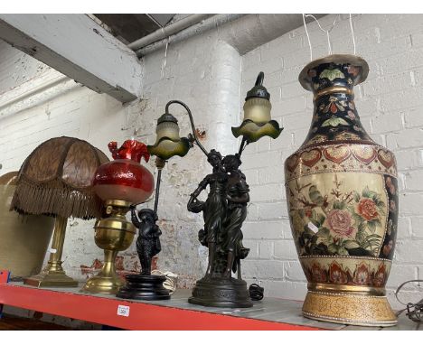 A large vase lamp, 2 figural lamps, a paraffin lamp with cranberry glass shade and funnel and a brass column lamp with shade.