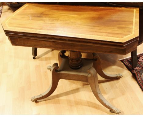 A Regency mahogany card table, crossbanded top enclosing a baize lined playing surface, ring turned column, sabre legs, brass