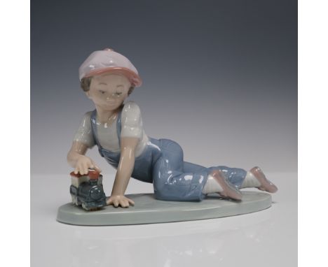 A young child with bright expression, dressed in soft blue overalls, a white short sleeve shirt, and pale pink cap. The child