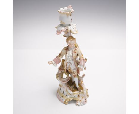 A delicate Continental porcelain candlestick figurine featuring a finely dressed gentleman in an eighteenth century style flo
