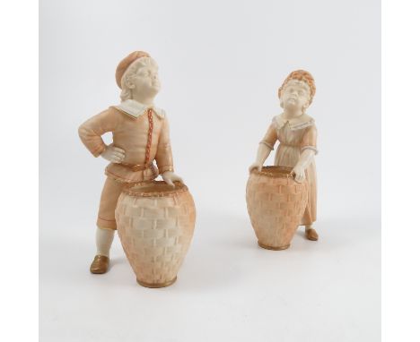 A pair of Royal Worcester blush ivory Kate Greenaway figures, modelled as a girl and a boy standing in front of wicker basket