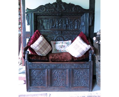 An antique oak box seat hall settle, having a recessed carved panel back with three carved panels below the seat, with scroll