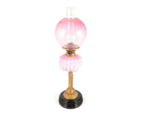 Victorian brass oil lamp, strawberry tinted opaque reservoir of moulded leaf design, raised on a column, black circular base,