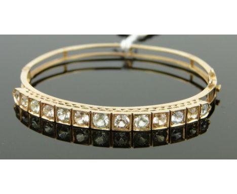 Unmarked gold hinged bangle
set with a row of coloured stones, 9.5g gross.