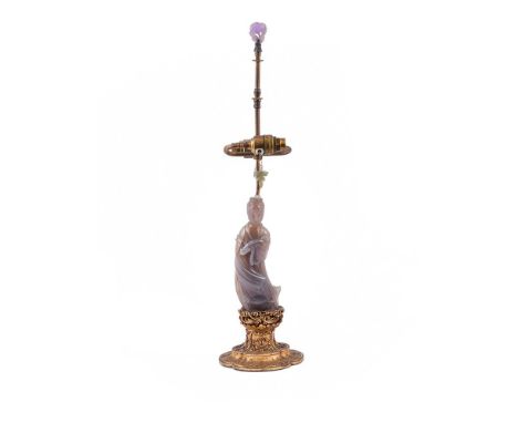 A Chinese agate figure of Guanyin, holding a ruyi sceptre, mounted on a carved gilt base, fitted for electricity with a brass