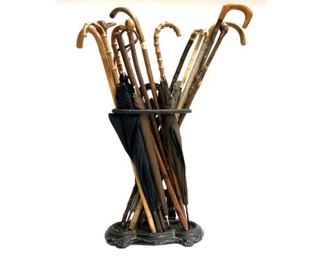 A cast iron stick stand containing a quantity of various walking sticks and vintage umbrellas 