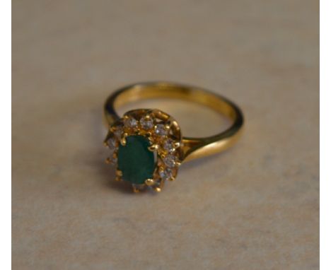 18ct gold emerald and diamond cluster ring, central oval emerald surrounded by smaller round diamonds, Ring Size K