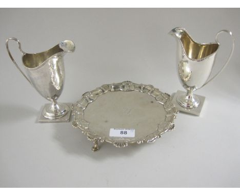 A George III silver Salver engraved crest, shaped rim on hoof feet, London 1762, repaired, and two helmet shape Cream Jugs on