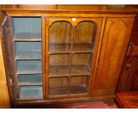 A LIGHT WOOD STANDING BOOKCASE having a centre six pane glazed door with cupboards either side, on bracket feet, 118 cms wide