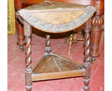 A CIRCA 1930 CARVED OAK CRICKET TABLE in triangular form with triple flaps opening to form a circular top, leaf carved to the